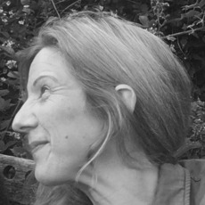 Schwarzweißfoto einer Frau mit langen Haaren im Profil, die im Freien sitzt, im Hintergrund Laub.