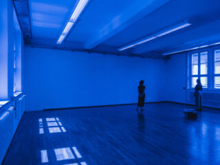 Ein in blaues Licht getauchter Raum mit zwei Personen.