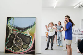 Eine Gruppe von Menschen steht in einer Kunstgalerie und betrachtet und diskutiert ein großes abstraktes Gemälde an der Wand.