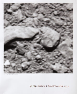 Eine unscharfe Schwarzweiß-Nahaufnahme einer felsigen Oberfläche mit dem handgeschriebenen Text „ALLERLEZTES REKONSTRUIERTES BILD“ am unteren Rand.