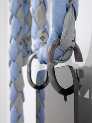 Nahaufnahme von zwei dicken, geflochtenen Seilen in Hellblau und Grau, die durch große Metallringe geschlungen sind, darunter ist ein Teil eines rechteckigen Spiegels sichtbar.