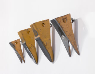 Auf weißem Untergrund sind vier metallische, keilförmige Objekte in absteigender Größe nebeneinander angebracht, deren Oberflächen rostfarben und schwarz lackiert sind.