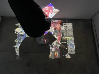 Person, die auf einem Betonboden steht, während in einem schwach beleuchteten Raum digitale Bilder und Grafiken auf den Boden und die Wand projiziert werden.