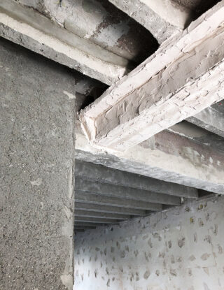 Sichtbare Betonbalken und unbehandelter Putz an einer Decke und Wand in einem im Bau oder in der Renovierung befindlichen Gebäude.