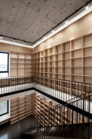 Eine moderne, leere Bibliothek mit hölzernen Bücherregalen an den Wänden, großen Fenstern und einer schwarzen Metalltreppe in der Mitte.