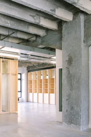 Ein modernes Interieur zeichnet sich durch freiliegende Betonbalken und -säulen, helle Holzregale, große Fenster und unfertige Deckenelemente mit sichtbarer Verkabelung aus.