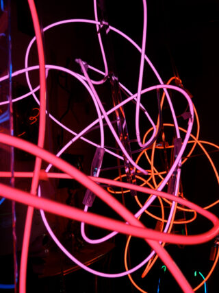 Verworrene Neonröhren in den Farben Rot, Pink und Orange leuchten vor einem dunklen Hintergrund.