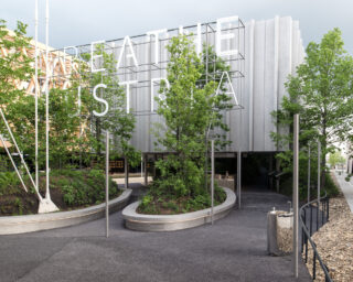 Modernes Gebäude mit großen weißen Buchstaben „BREATHE AUSTRIA“ über einem Eingang, umgeben von grünen Bäumen und geschwungenen Gehwegen.