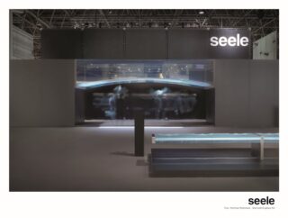Ein moderner Messestand mit einer großen schwarzen Wand mit dem „seele“-Logo, transparenten Installationen und einer Sitzbank im Vordergrund.