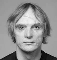 Eine Person mittleren Alters mit heller Haut und glattem, hellem Haar, die vor einem schlichten Hintergrund direkt in die Kamera blickt.