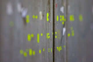 Nahaufnahme einer grauen Oberfläche mit vereinzelten gelben Markierungen und abgenutzten weißen Flecken, die in der Mitte durch eine vertikale Naht geteilt ist.