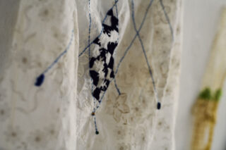 Eine Nahaufnahme von weißem Spitzenstoff mit blauen Fäden darin und einem schwarz-weiß gemusterten rautenförmigen Flicken in der Mitte.