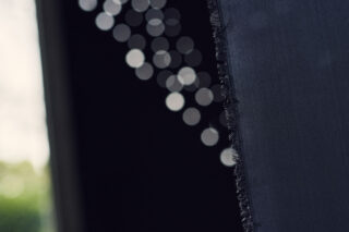 Nahaufnahme einer rauen, zerrissenen Stoffkante mit verschwommenen kreisförmigen Lichtern im dunklen Hintergrund.