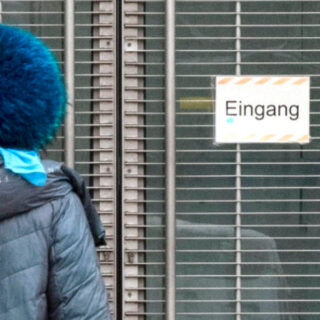 Person mit blauem Hut steht vor einer Glastür mit einem Schild mit der Aufschrift „Eingang“.