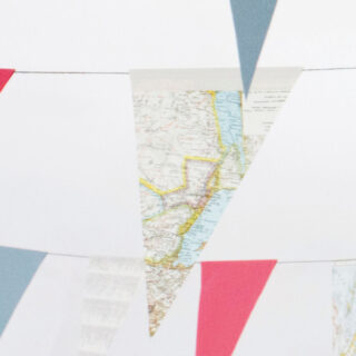 Dreieckige Papiergirlanden in Blau, Rot und mit Kartenaufdruck sind auf einem hellen Hintergrund aufgereiht.