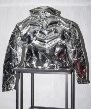 Eine metallisch silberne Pufferjacke, die auf einem Ständer vor einem schlichten weißen Hintergrund präsentiert wird.
