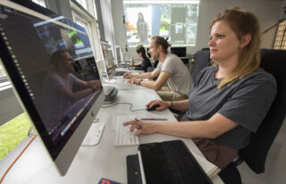 Eine Gruppe von Personen arbeitet an Desktop-Computern in einem Büro und konzentriert sich auf die auf ihren Monitoren angezeigte 3D-Modellierungssoftware.