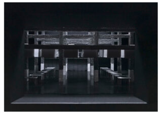 Ein schwach beleuchteter Innenraum mit Hockerreihen und rechteckigen Säulen, von einem dunklen Eingang oder Fenster aus betrachtet.