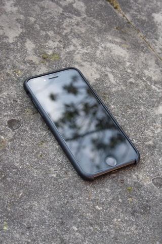 Ein schwarzes Smartphone mit spiegelndem Bildschirm liegt mit der Vorderseite nach oben auf einer rauen, grauen Steinoberfläche.