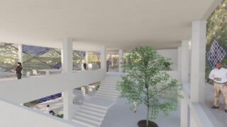 Geräumiges, modernes Gebäude mit weißen Wänden, zentraler Treppe, Baum im Innenbereich und Menschen, die überall herumstehen. Große Fenster bieten Blick auf Grünflächen und Solarmodule.