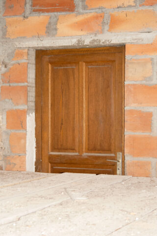 Eine Holztür ist unten teilweise durch eine Betonfläche blockiert, die in eine unfertige Ziegelwand eingelassen ist.