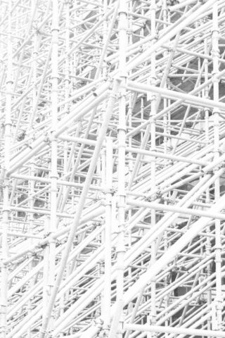 Dichtes Netzwerk aus weißen Metallgerüstrohren und -verbindungen, die auf einer Baustelle ein geometrisches Muster bilden.