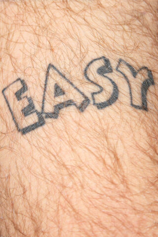 Eine Tätowierung des Wortes „EASY“ in fetten, umrandeten Buchstaben auf einem Stück behaarter Haut.