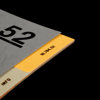 Eine Nahaufnahme eines gelben Aktenordners, der teilweise mit einem grauen Dokument bedeckt ist. Auf dem Ordner ist die Nummer 10.794.52 aufgedruckt.