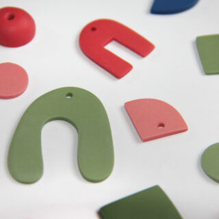 Verschiedene flache, bunte Polymer-Tonformen mit Löchern, angeordnet auf weißem Hintergrund.