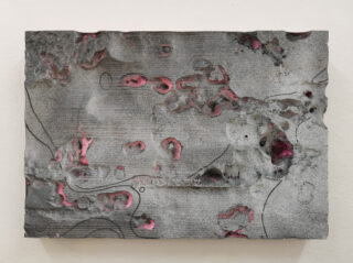 Eine rechteckige Platte mit einer rauen, narbigen grauen Oberfläche und vereinzelten rosa Vertiefungen sowie schwachen schwarzen Linien und kreisförmigen Markierungen.