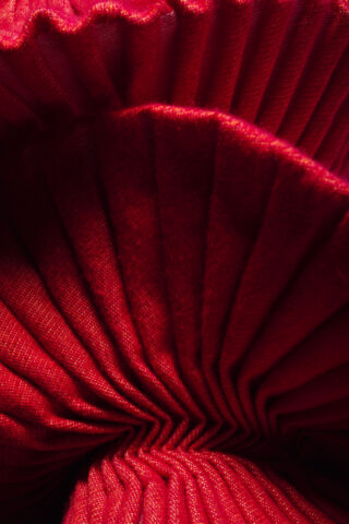 Nahaufnahme eines roten Plisseestoffs mit sichtbarer Textur und Falten, die ein abstraktes Muster erzeugen.