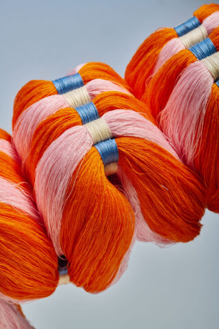 Bündel aus orangefarbenem, rosa und blauem Faden sind ordentlich in Reihen auf einem hellen Hintergrund angeordnet.