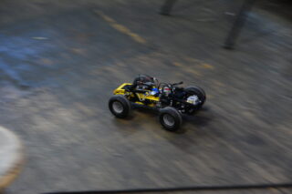 Ein ferngesteuertes Auto im gelb-schwarzen Design fährt schnell über eine glatte Indoor-Oberfläche.