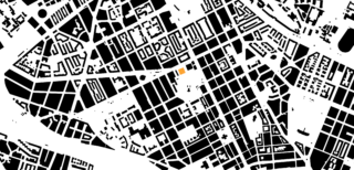 Schwarzweißkarte mit detaillierten Straßen und Gebäuden der Stadt, wobei zwei kleine farbige Rechtecke in der Nähe der Mitte bestimmte Standorte anzeigen.