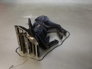 Auf einer flachen Oberfläche ist ein schwarzes 3D-gedrucktes Modell eines ruhenden Tieres, möglicherweise eines Kalbs, mit sichtbaren Stützstrukturen abgebildet.