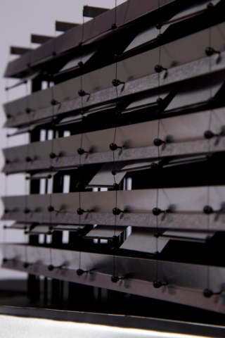 Nahaufnahme eines modernen Architekturmodells mit mehreren horizontalen schwarzen Lamellen, die durch vertikale Stäbe und kugelförmige Verbindungsstücke zusammengehalten werden.