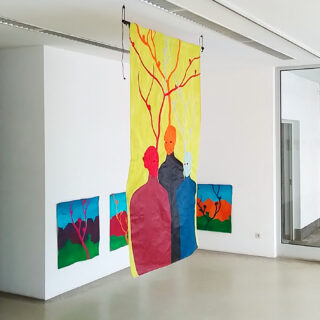 In einem modernen Galerieraum mit weißen Wänden werden farbenfrohe Gemälde und ein großes hängendes Stoffstück mit abstrakten menschlichen Figuren und Ästen ausgestellt.