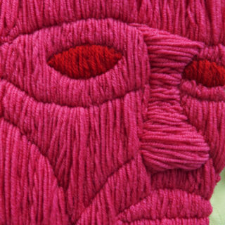 Nahaufnahme eines Textilkunstwerks, das ein stilisiertes menschliches Gesicht aus rosa und rotem Garn zeigt, das in strukturierten, gestickten Mustern angeordnet ist.