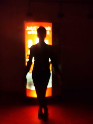 Die Silhouette einer Person steht in einem dunklen Raum vor einem hell erleuchteten Verkaufsautomaten.