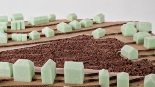 Modell einer Landschaft mit grünen Schaumstoffformen, die Gebäude darstellen, braunem strukturiertem Material als Gelände und geschichtetem Karton, der die Topografie simuliert.