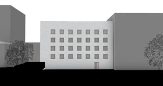 Ein weißes rechteckiges Gebäude mit fünf Fensterreihen, einer einzelnen Tür unten rechts und benachbarten grauen Gebäuden auf beiden Seiten. Im Vordergrund sind zwei Bäume zu sehen.