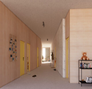 Ein Flur mit hellen Holzwänden, gelben Türrahmen, verstreuten Schuhen, einem Teddybären auf einem Regal und Sonnenlicht, das aus einem Zimmer am Ende fällt.