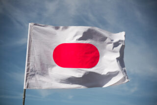 Eine weiße Flagge mit einem großen roten Oval in der Mitte, die vor einem blauen Himmel weht.