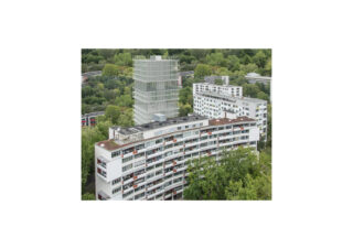 Luftaufnahme moderner weißer Wohnhäuser, umgeben von Bäumen, mit einem höheren Glasgebäude im Hintergrund.