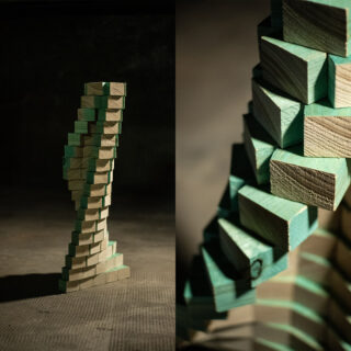 Zwei Fotos eines gestapelten, sich windenden Turms aus rechteckigen Holzblöcken mit grünen Kanten, der bei schwacher Beleuchtung auf einer strukturierten Oberfläche steht.