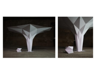 Zwei geometrische weiße Skulpturen auf strukturierter Oberfläche; die größere hat eine breite, eckige Oberseite und eine schmale Basis, während die kleinere ein facettiertes Polygon darstellt. Der Hintergrund ist dunkel und industriell.