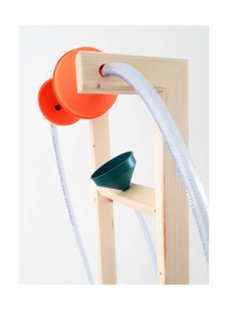 Ein Holzrahmen hält oben zwei orangefarbene Trichter und darunter einen grünen Trichter, die durch durchsichtige Kunststoffschläuche verbunden sind, vor einem schlichten weißen Hintergrund.