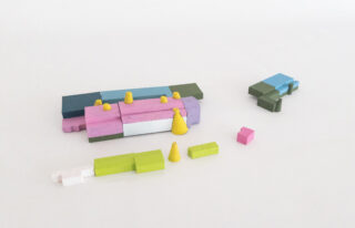 Verschiedene bunte Holzklötze und -kegel, in kleinen Gruppen auf einer weißen Oberfläche angeordnet.