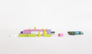 Bunte geometrische Holzblöcke, darunter Rechtecke, Quadrate und Kegel, sind auf einer weißen Oberfläche angeordnet, wobei einige gruppiert und andere getrennt sind.