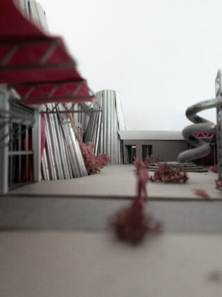 Architekturmodell mit metallischen, zylindrischen Strukturen, einer Spiralrutsche, rosa Laub und einem Betonweg, der zu einem Gebäude führt.